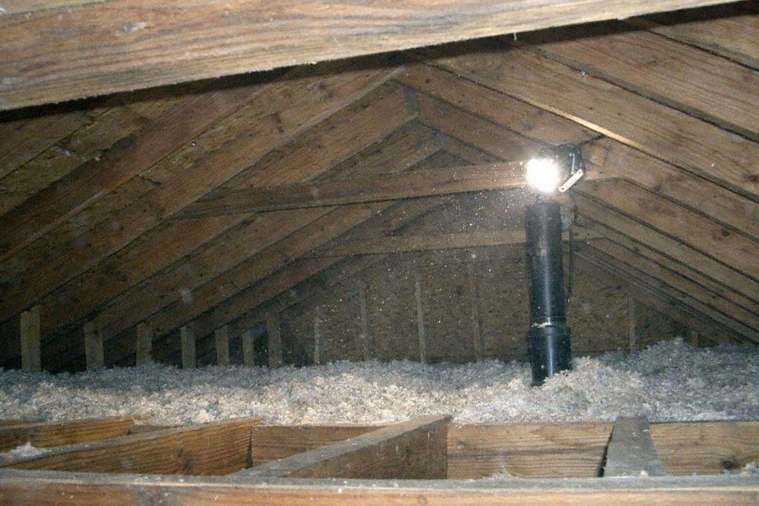 Rafters and decking of a ventilated attic under a clipped work light, blown insulation between the joists