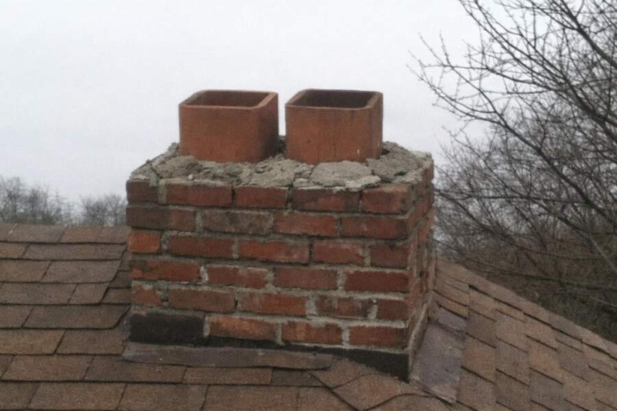 The open clay flue of an uncapped brick chimney above a shingle roof