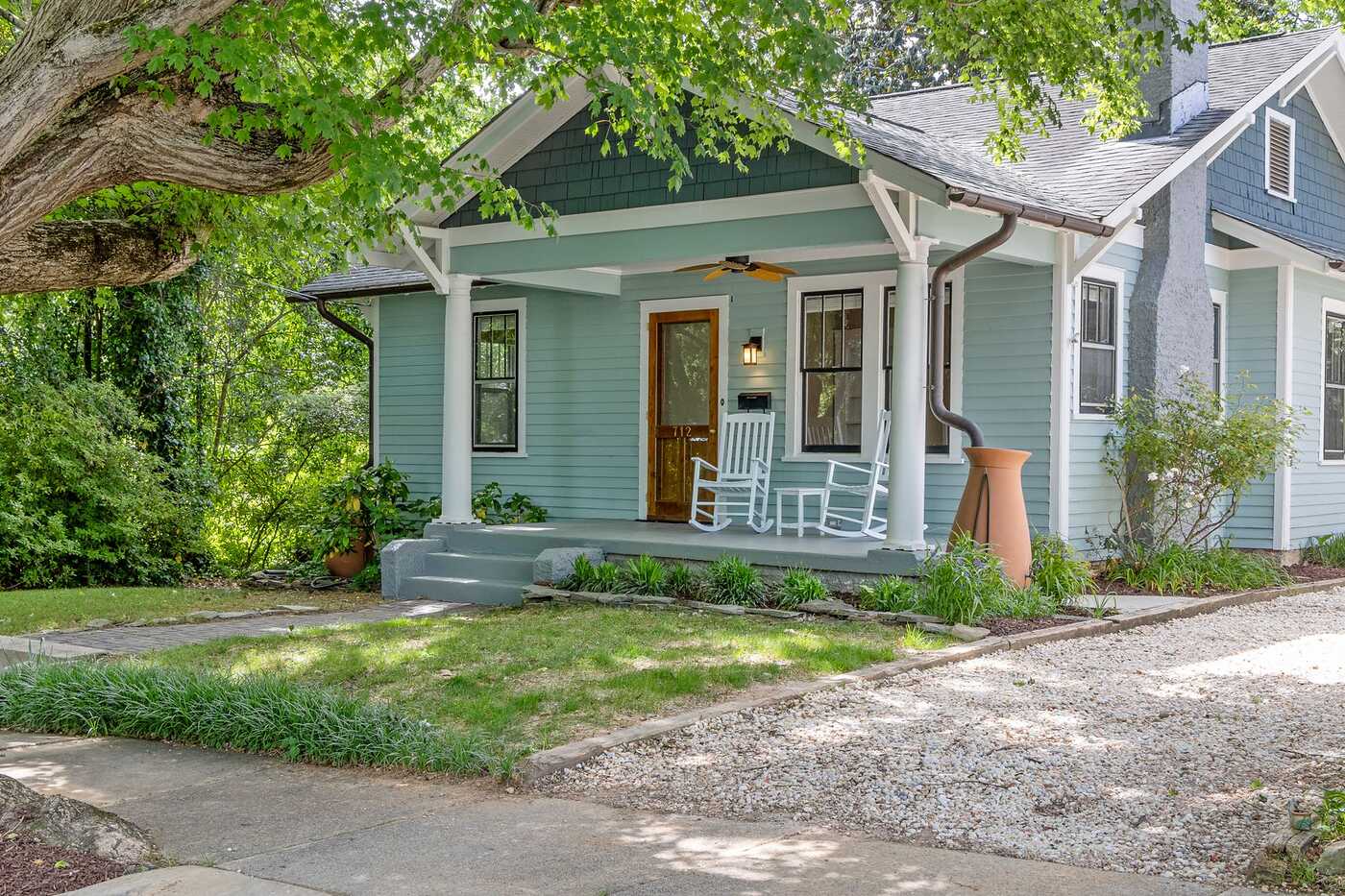 A pale blue craftsman bungalow with a deep porch and rocking chairs