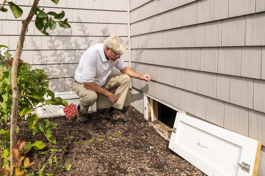 An inspector crouched at a crawl space access door in the side of a house