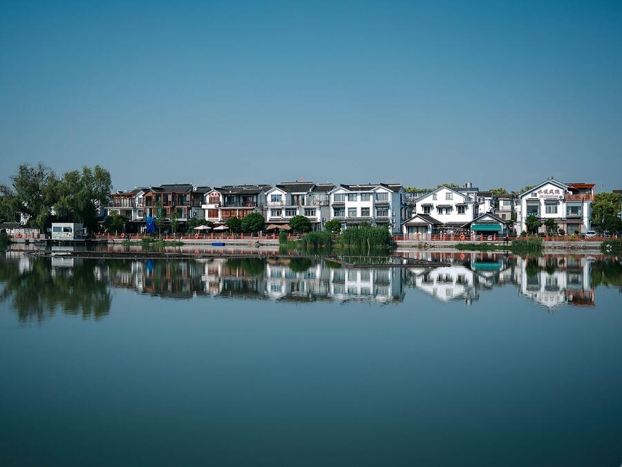 Houses reflected in calm lake water under a clear sky