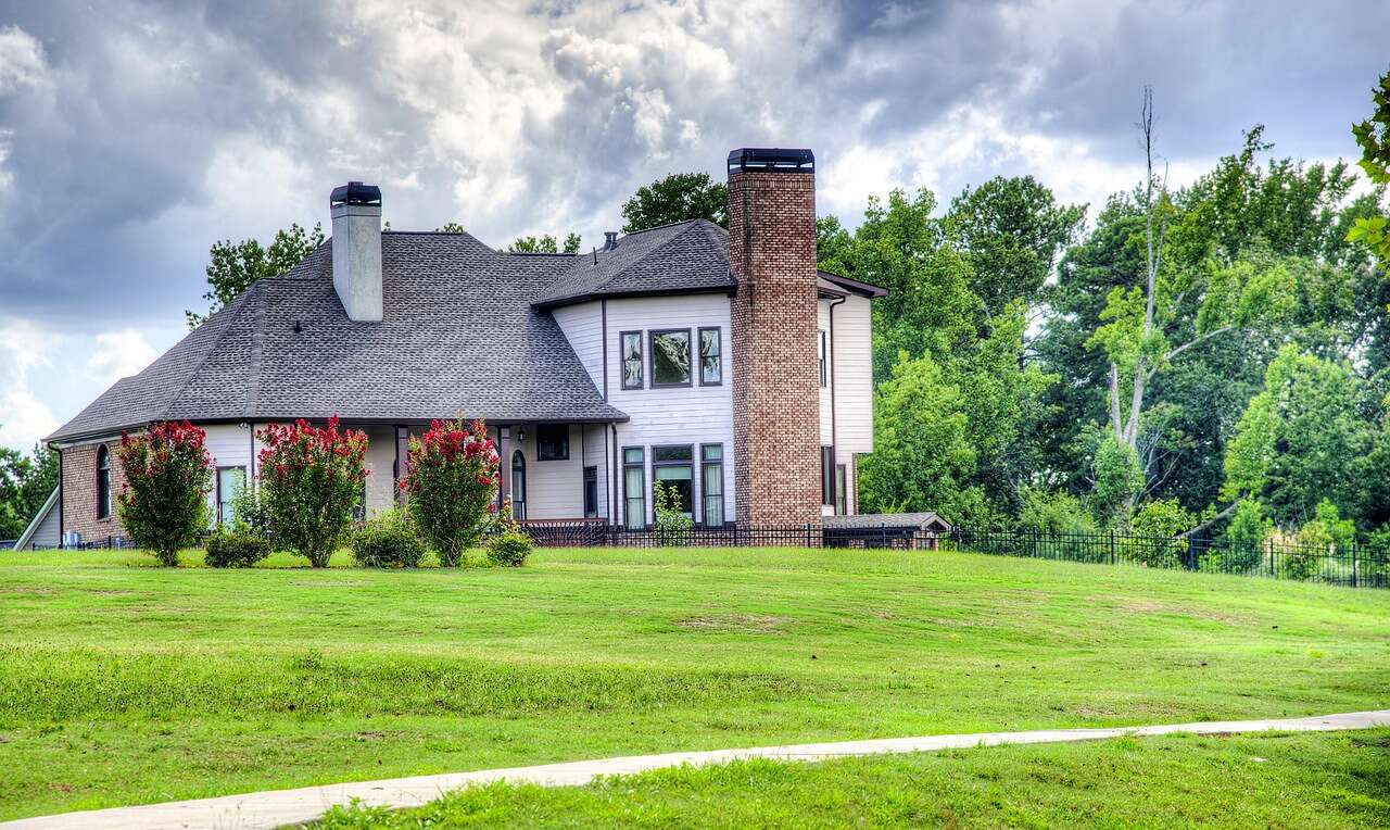 A two-story brick house with a chimney and lawn beside a pond