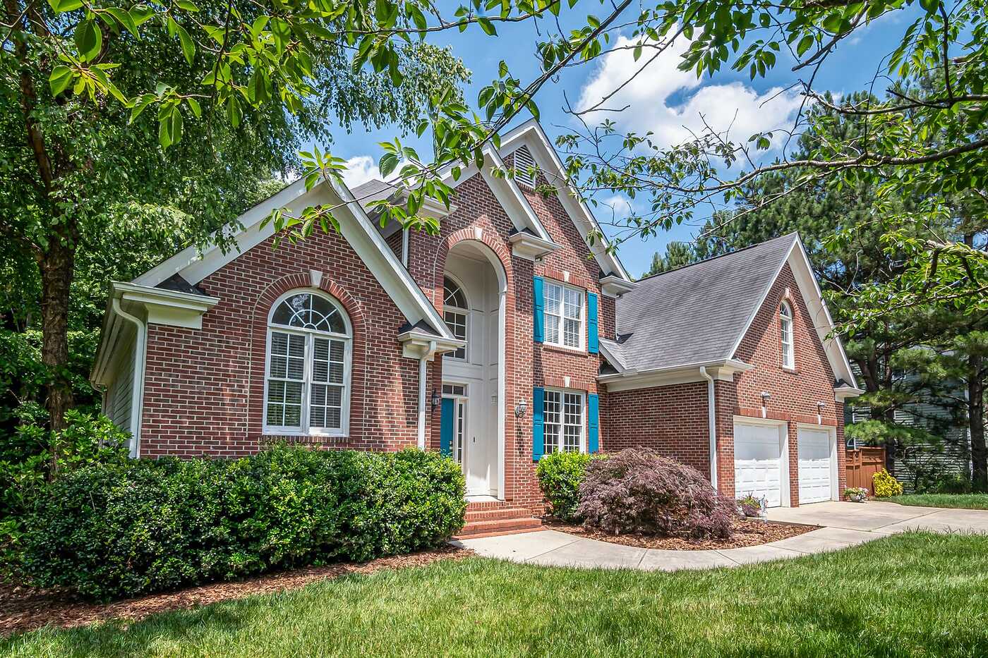 A brick house with a composition shingle roof, arched windows and trees close to the eaves