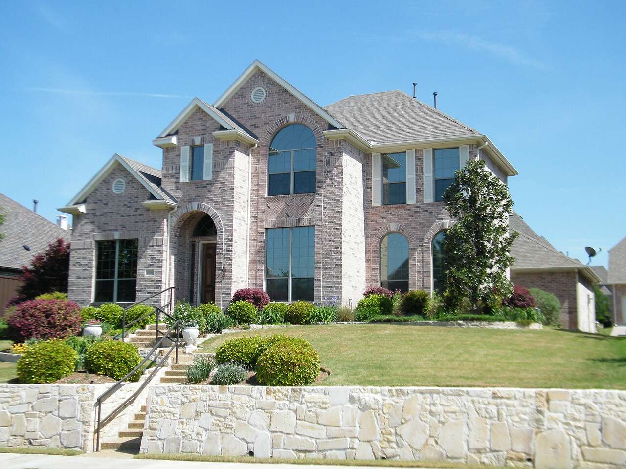 A large two-story house of brick and stone with a stone retaining wall